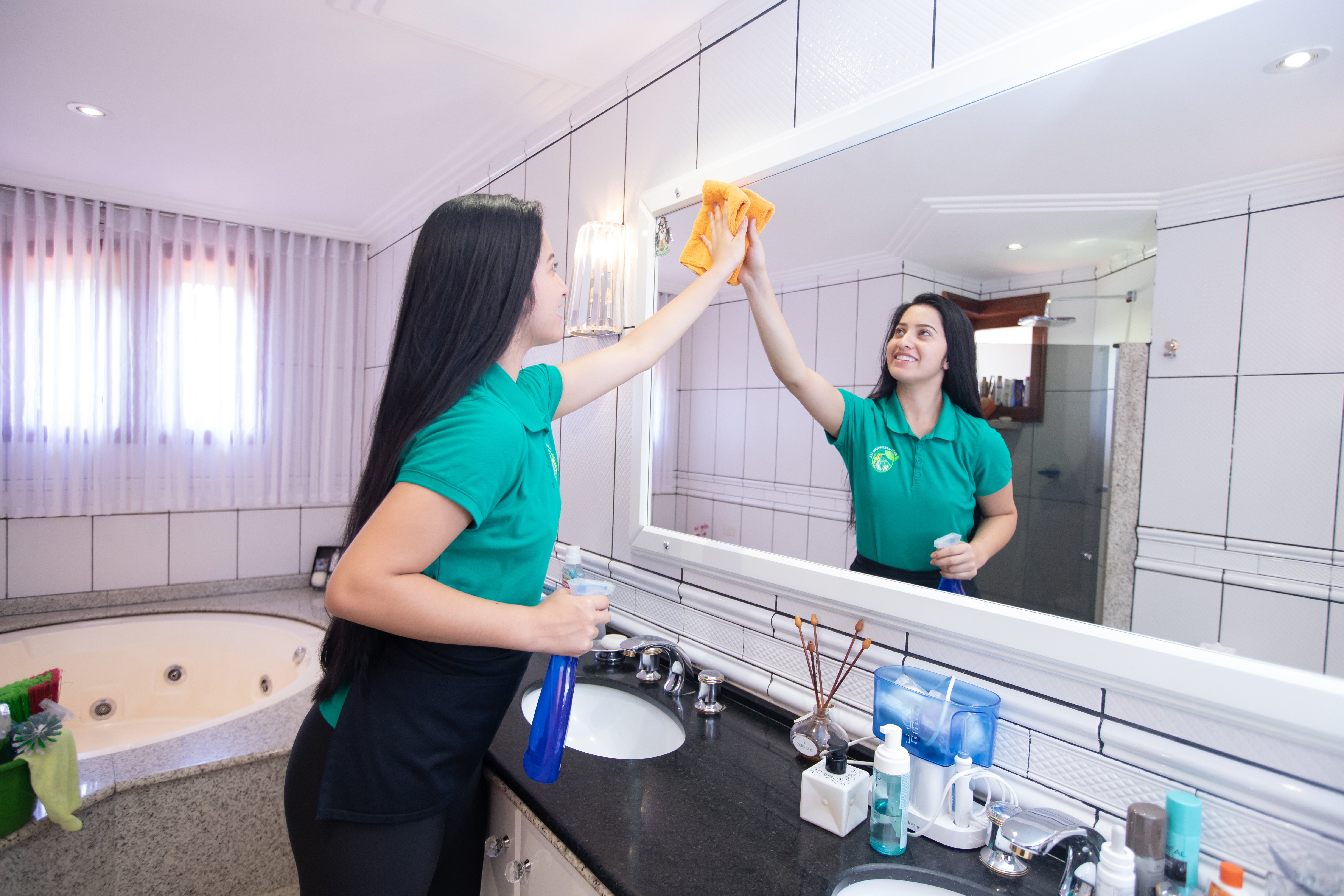 Professional cleaner wiping a bathroom mirror with a yellow microfiber cloth, ensuring a spotless and gleaming surface.