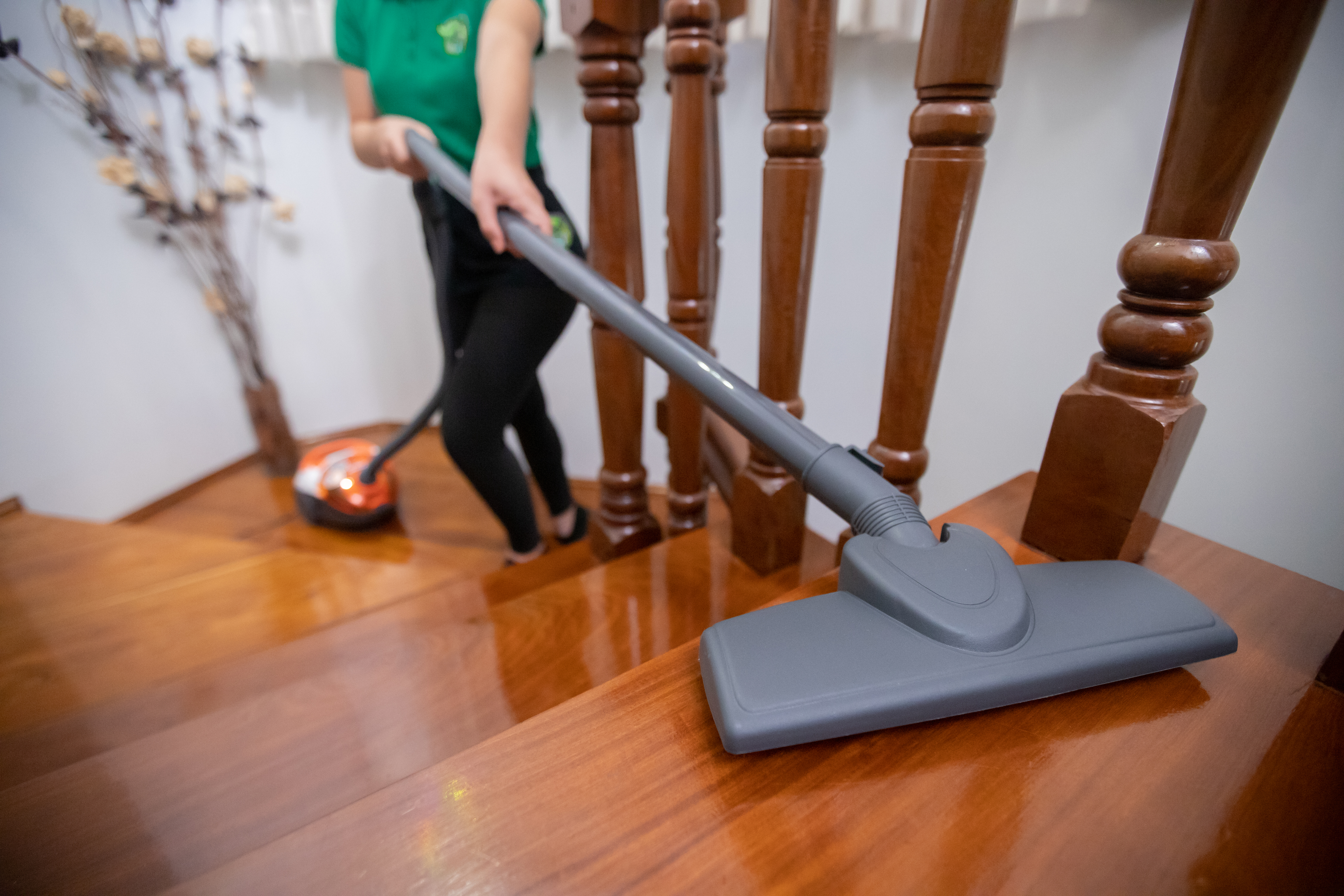 Professional cleaner vacuuming wooden stairs using a high-powered vacuum, ensuring a spotless and dust-free home.