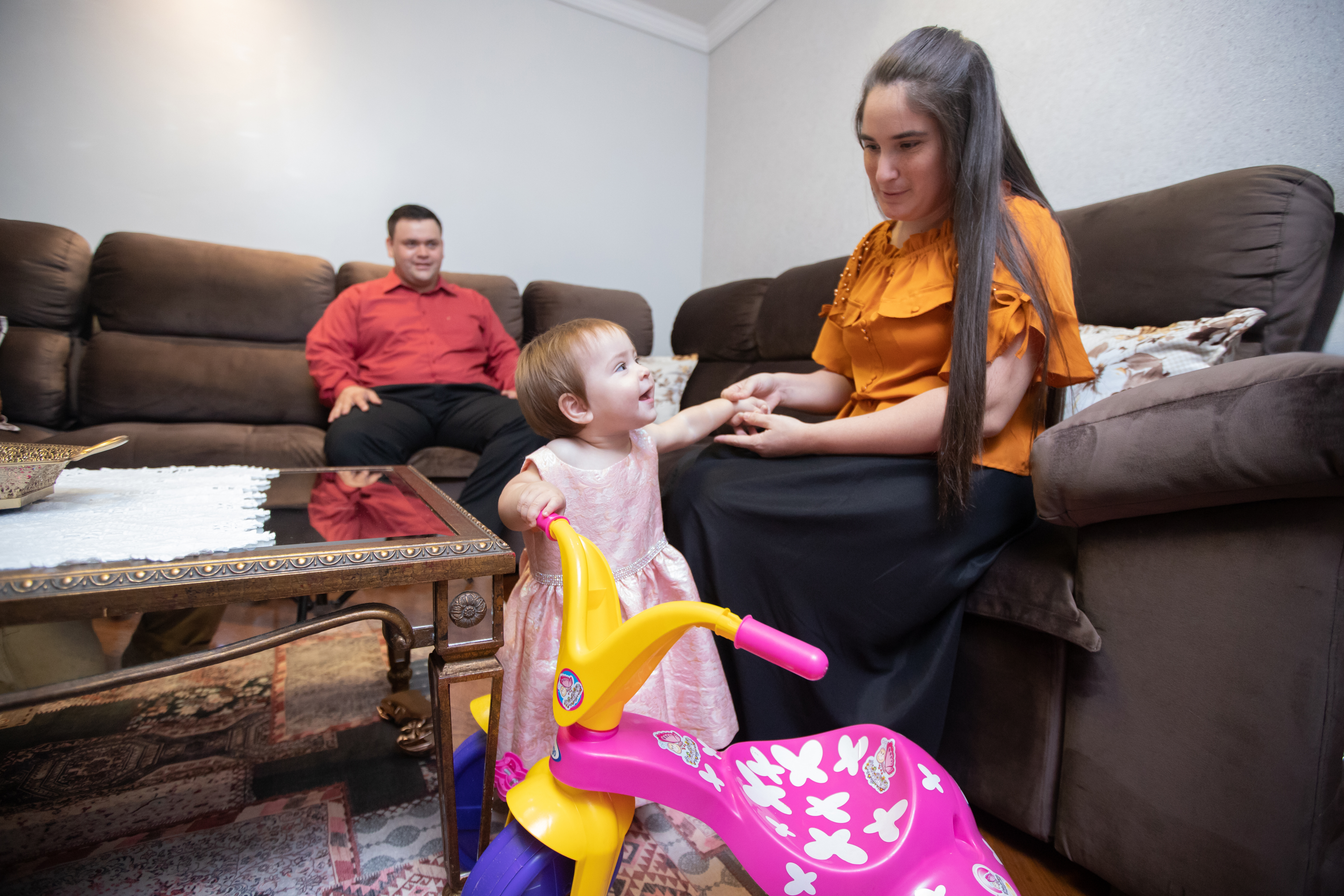 A tidy, welcoming living room showcasing a peaceful family moment—a smiling toddler engages happily with her mother, as the father watches warmly from the background. The clean, organized space emphasizes the idea that a clean home nurtures clarity, connection, and joyful interactions, perfectly reflecting how a clean environment supports a clear, stress-free mindset.