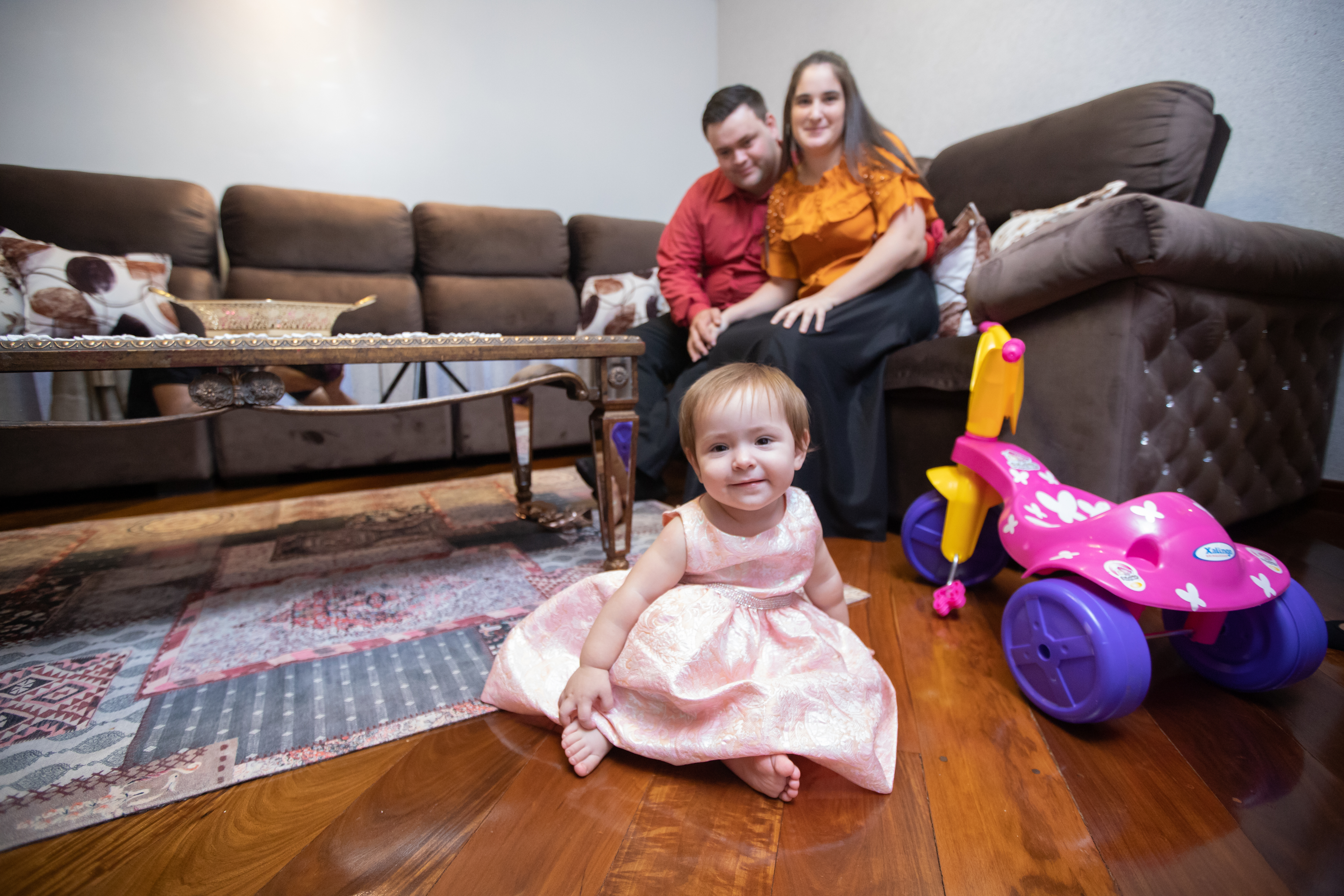 Happy family enjoying a clean and organized living room with a toddler playing on the spotless hardwood floor—highlighting the benefits of maintaining a tidy and healthy home environment.