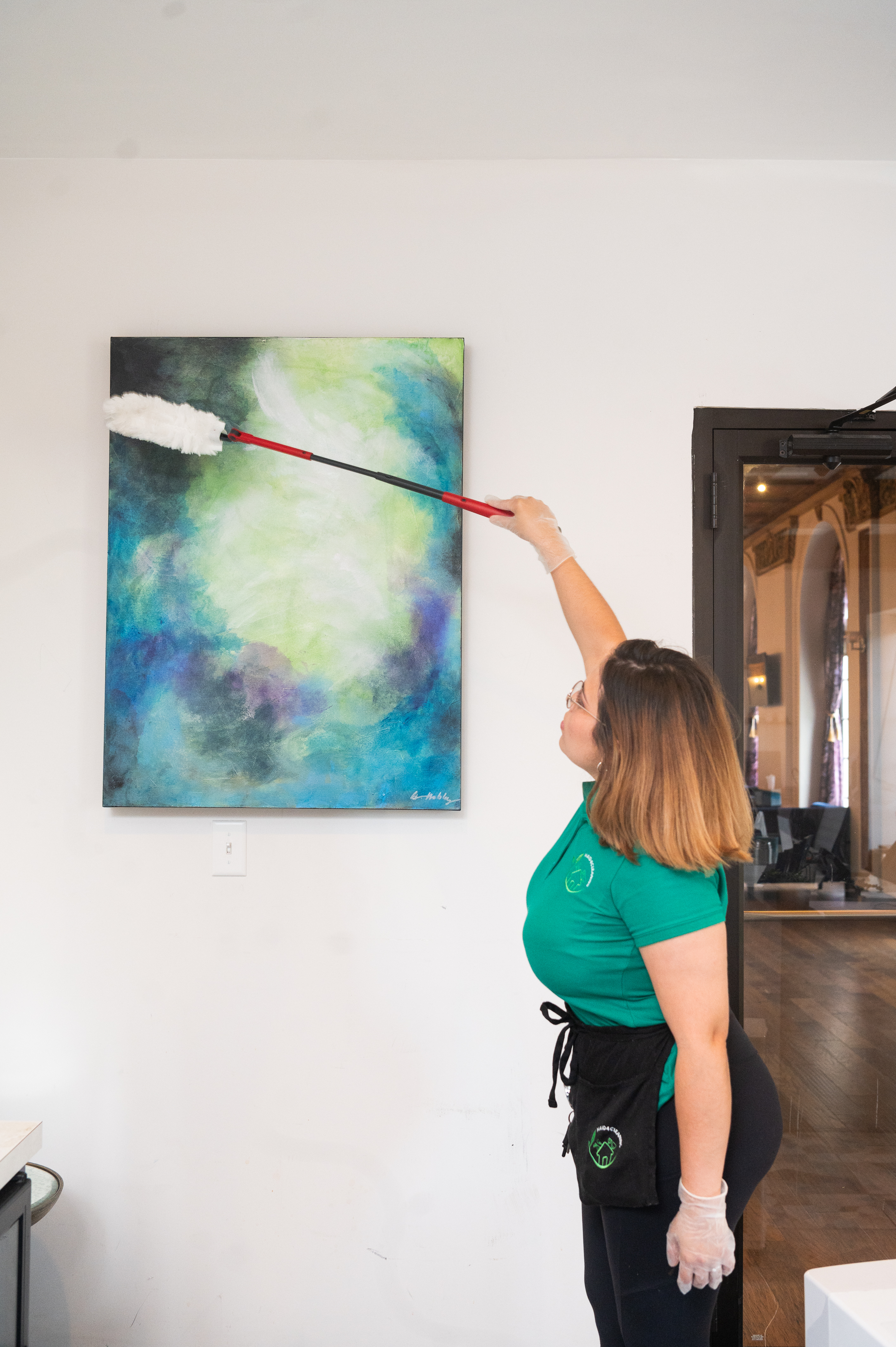 A professional cleaner from Maid 4 Cleaning in Saint Louis dusting a high surface using an extendable duster, demonstrating the importance of dusting from top to bottom for an efficient cleaning routine.