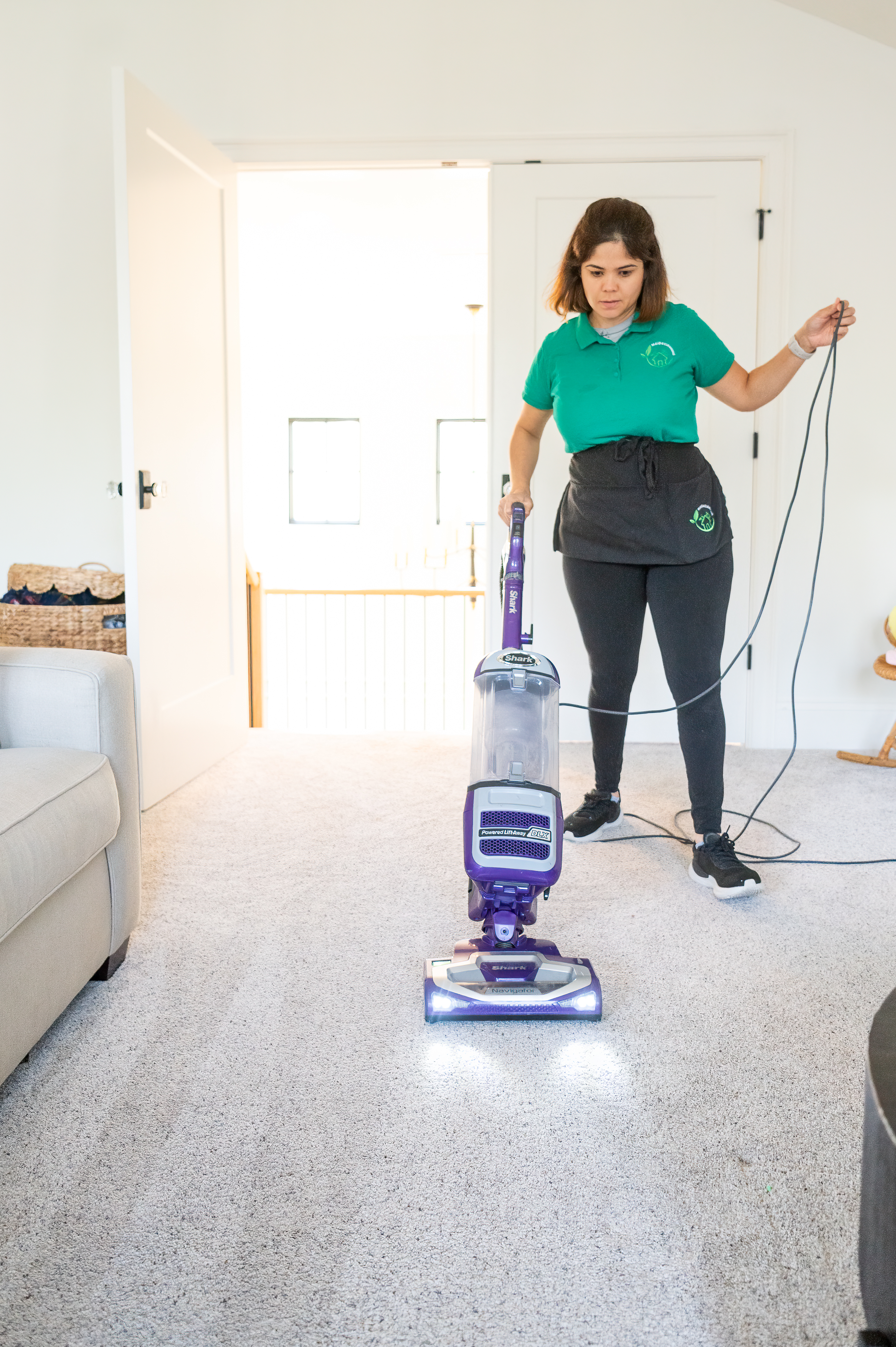 A professional cleaner from Maid 4 Cleaning vacuums a light-colored carpet in a modern home, ensuring a spotless and fresh environment.