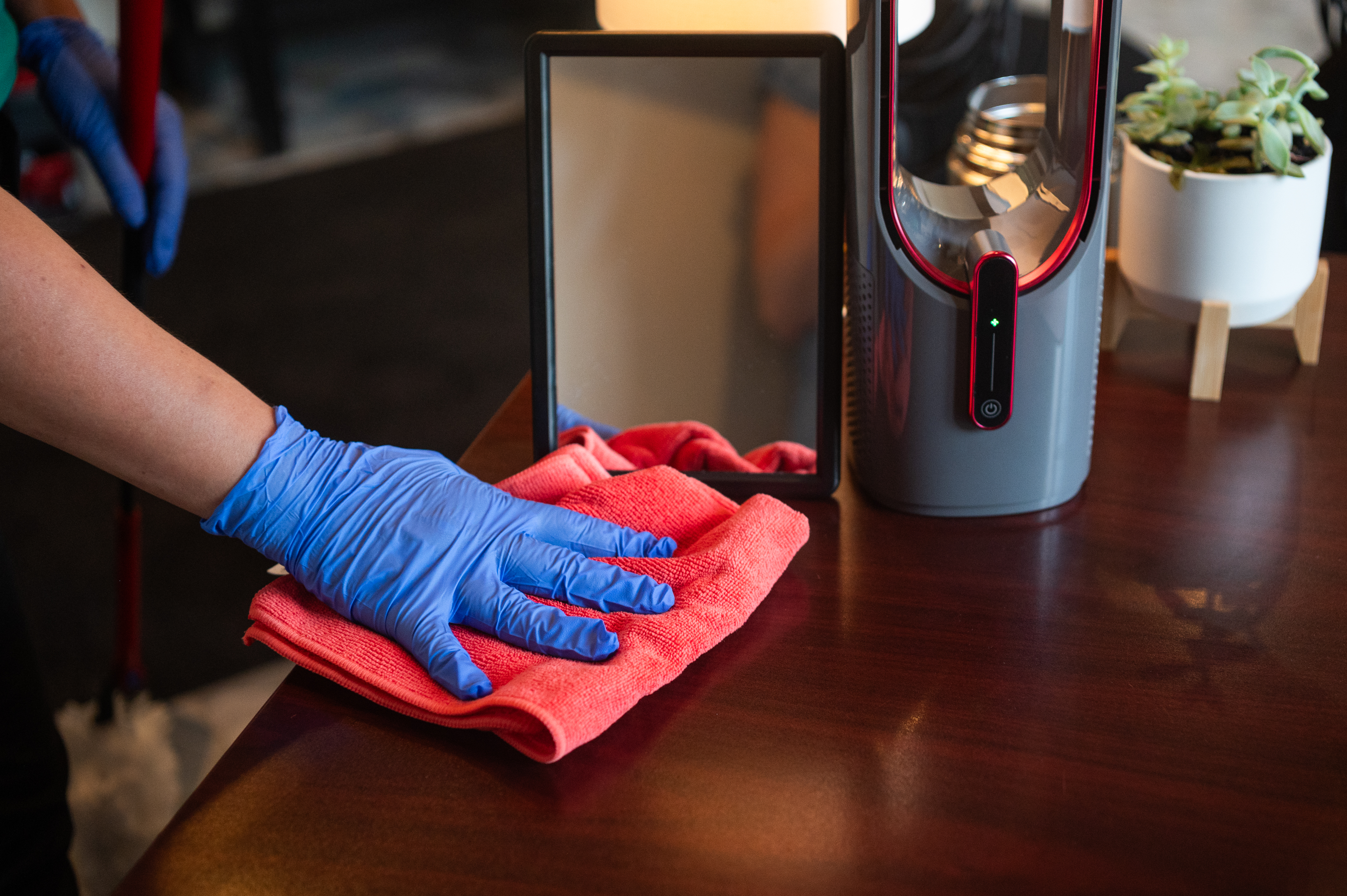 A professional cleaner wearing blue gloves wipes a wooden surface with a red microfiber cloth, ensuring a streak-free finish on a mirror. Proper cleaning techniques, such as using the right tools and avoiding excess product, help maintain a spotless home efficiently.