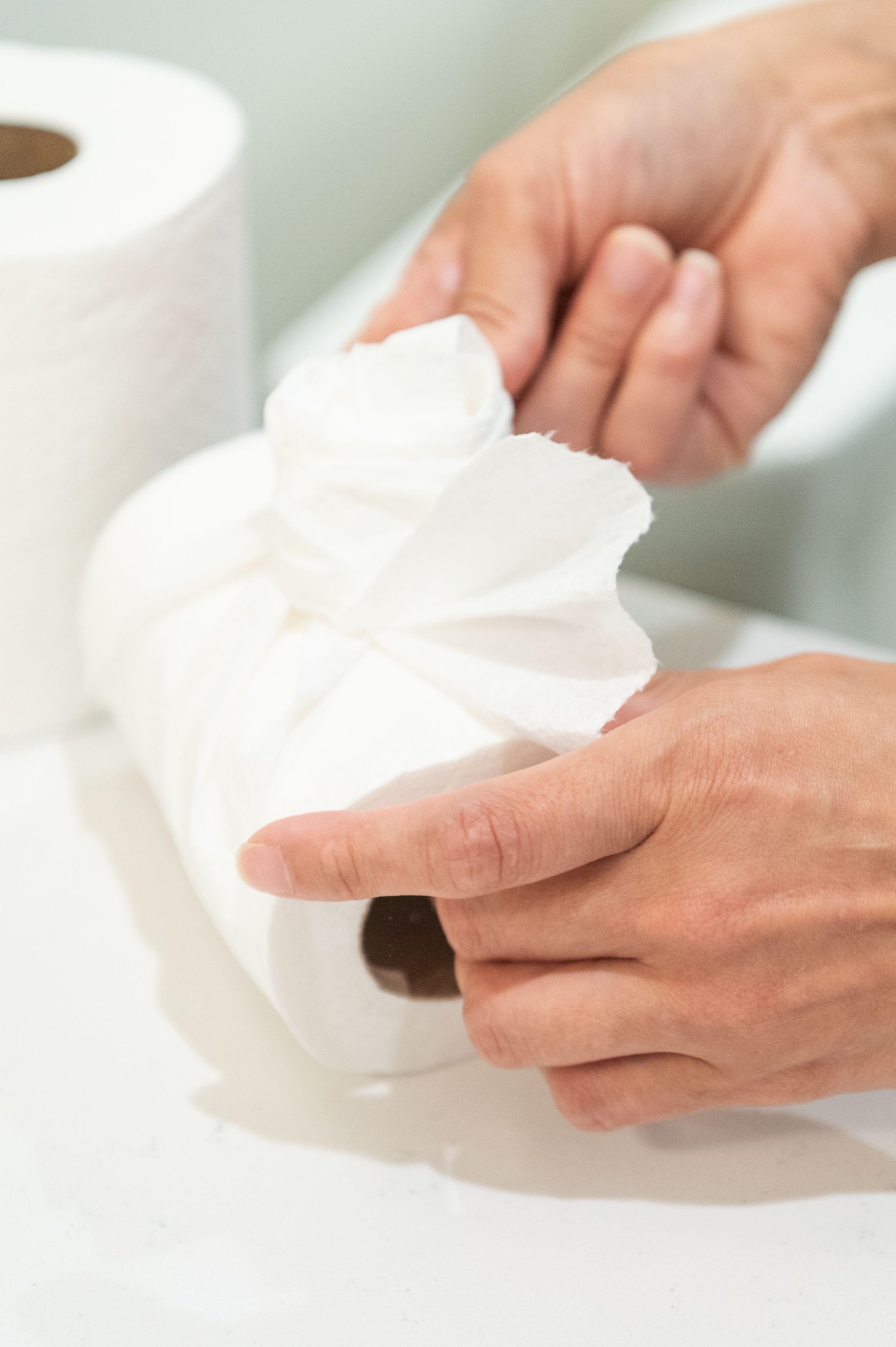 Close-up of hands pulling a sheet from a fresh roll of paper towels, emphasizing the importance of stocking up on cleaning essentials for a fresh start in January.